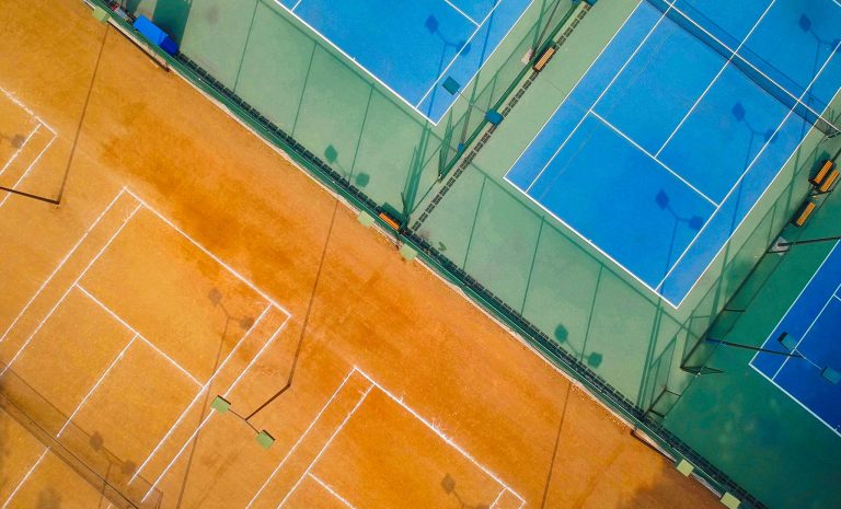 Photo of clay tennis courts and hard courts side by side, showcasing the different types of tennis court surfaces.